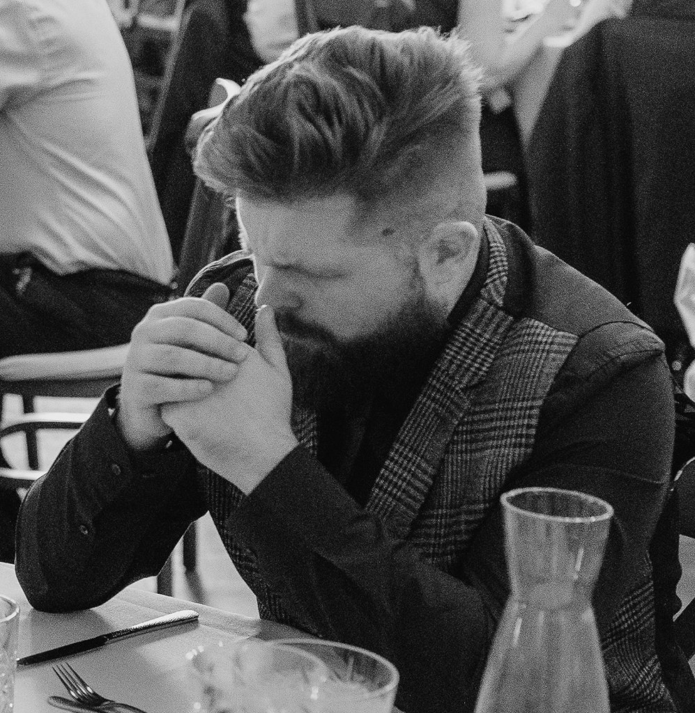 Dave Brown at a table, looking down, hands clasped.